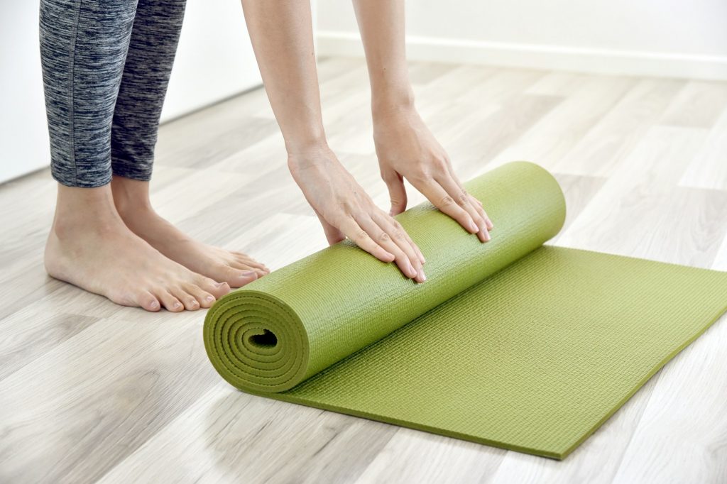 Woman folding yoga or fitness mat after working out at home, Home exercise workout.